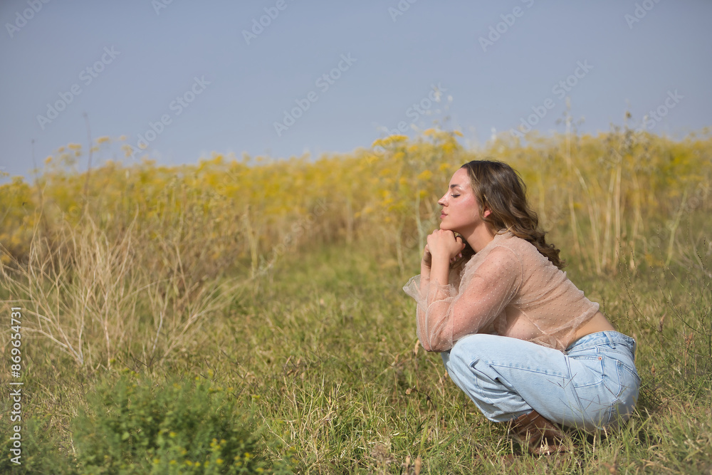 Young woman, beautiful, blonde, eyes closed, wearing jeans, silk shirt and cowboy boots, squatting in the middle of a field, relaxed, dreaming and at peace. Concept beauty, countryside, peace, nature. Young woman, beautiful, blonde, eyes closed, wearing jeans, silk shirt and cowboy boots, squatting in the middle of a field, relaxed, dreaming and at peace. Concept beauty, countryside, peace, nature.