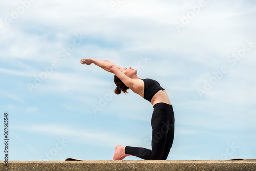 Sporty woman kneeling doing a backbend exercise, yoga outdoors photo