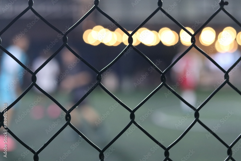 Fototapeta premium Mini soccer field with fence and blurred players in the background, selective focus 