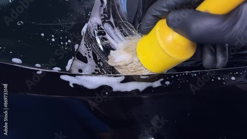 Car wash or car detailing studio employee carefully cleans hard-to-reach areas with a brush