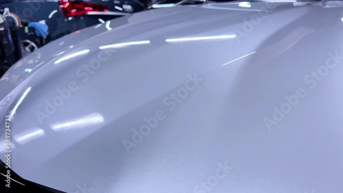 car wash or car detailing studio employee applies a ceramic or graphene coating to the paint of a white car