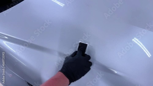 car wash or car detailing studio employee applies a ceramic or graphene coating to the paint of a white car