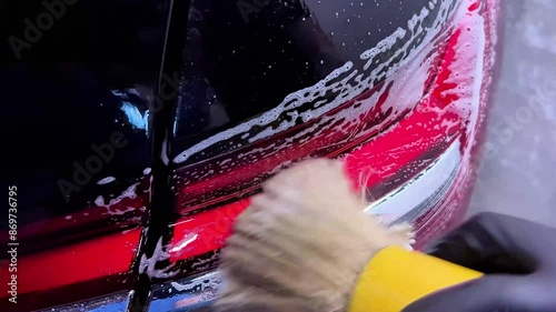 car wash or car detailing studio employee carefully washes the area around the car's rear light with a brush