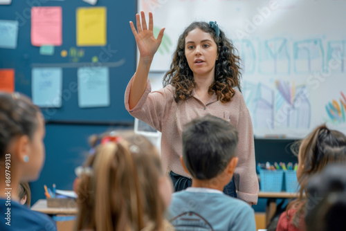 Young female teacher in front of the children giving the lesson next to a whiteboard in a school classroom. Kids looking and listening to the teacher.
