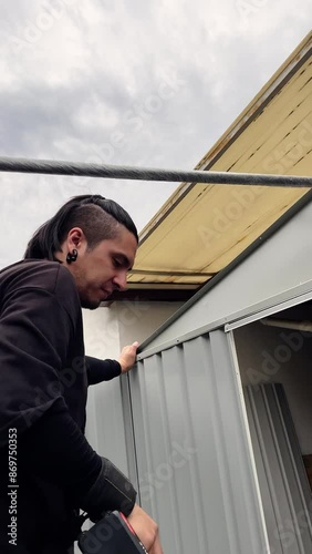 Building a metal warehouse: young man assembling and drilling in backyard