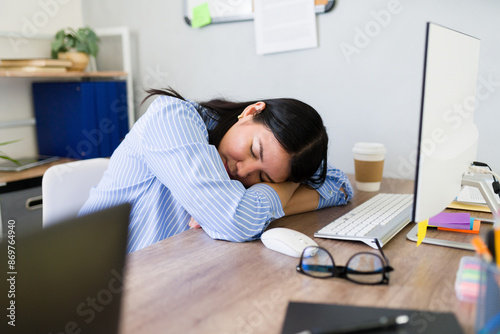 Exhausted young woman takes a power nap at her messy desk, illustrating the toll of a hectic workday