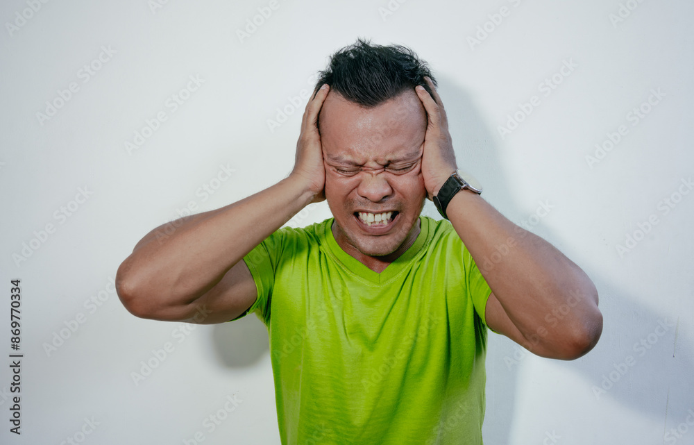 Asian man showing stress expression. Angry and mad face of Asian man in green t-shirt on isolated background Asian man showing stress expression. Angry and mad face of Asian man in green t-shirt on isolated background