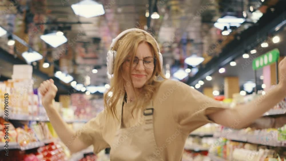 An enthusiastic employee, wearing a supermarket uniform, is joyfully dancing in the aisle with headphones on. They seem to be enjoying their work and showing positive energy An enthusiastic employee, wearing a supermarket uniform, is joyfully dancing in the aisle with headphones on. They seem to be enjoying their work and showing positive energy