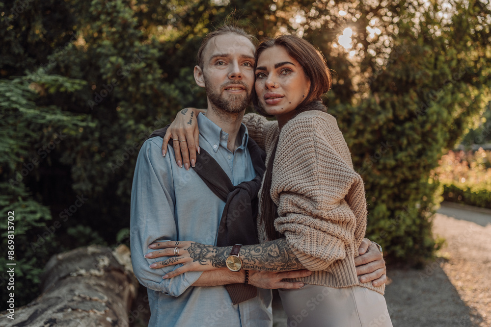 Fototapeta premium Smiling tattooed girl hugging her boyfriend in a park. Pretty redhead woman with tattoos and man on a walk.