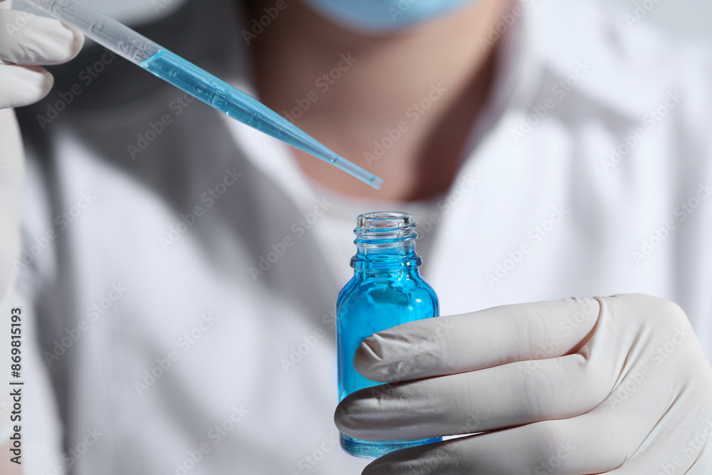 Scientist dripping liquid from pipette into glass bottle, closeup Scientist dripping liquid from pipette into glass bottle, closeup
