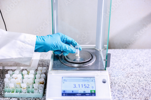 Fotografie A scientist's gloved hand is weighing a sample contained in a vial using a digital analytical balance with four-decimal precision, which is used in laboratory scientific, scientific research