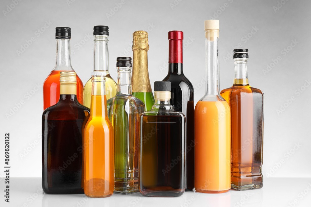 Bottles of different alcoholic drinks on white table against light background Bottles of different alcoholic drinks on white table against light background