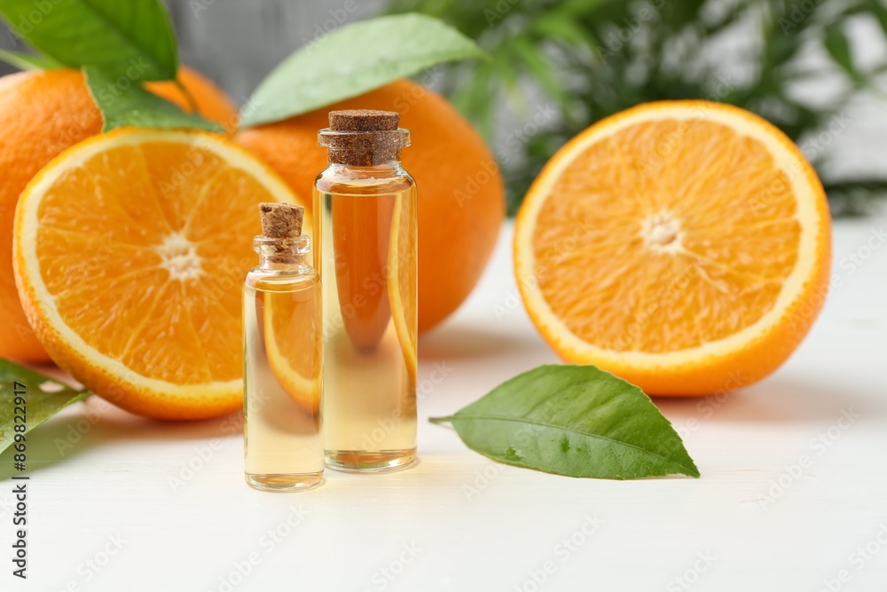Essential oils in bottles, oranges and green leaves on white table Essential oils in bottles, oranges and green leaves on white table