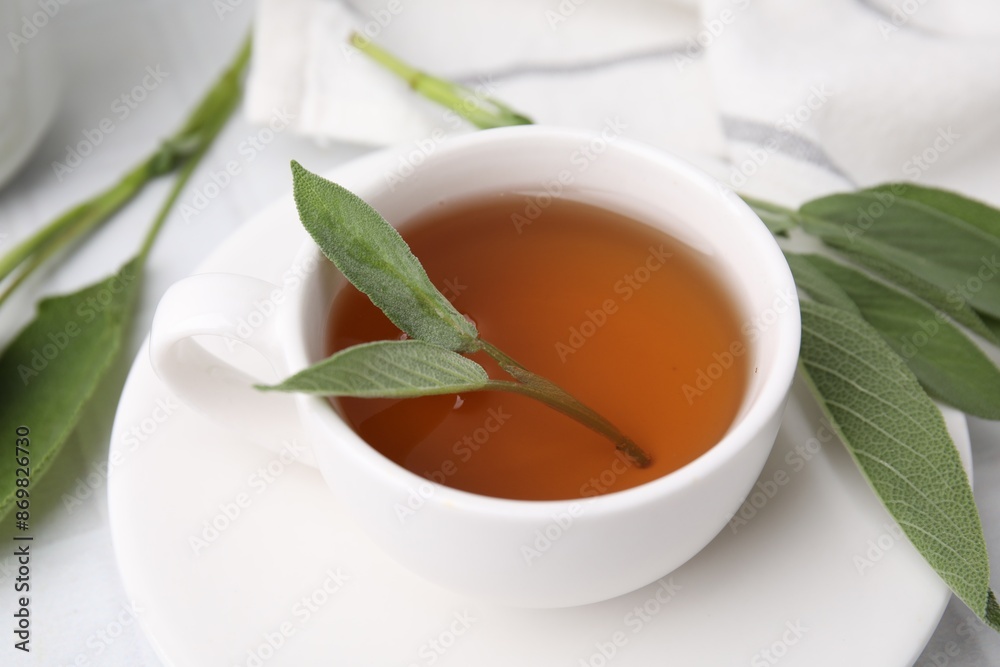 Aromatic herbal tea in cup with sage on white table Aromatic herbal tea in cup with sage on white table
