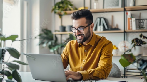 Handsome man working on a laptop in a well-organized home office, with a simple and clean background, dressed in casual business attire, highlighting the productivity and comfort of remote work 
