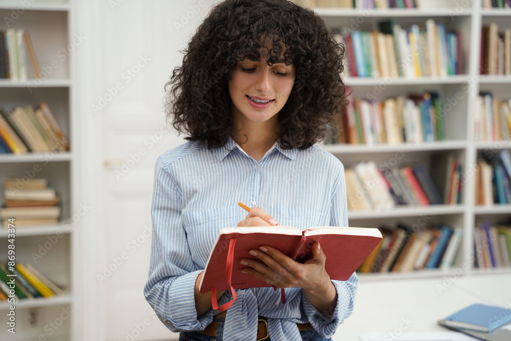 Woman student writing in her organizer preparing for classes in university library Woman student writing in her organizer preparing for classes in university library