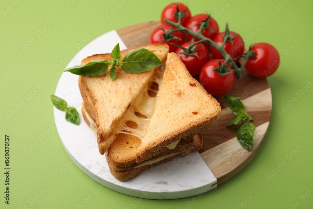 Pieces of toasted bread with melted cheese, tomatoes and basil on green background