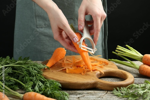 Woman peeling fresh carrot at wooden table, closeup photo