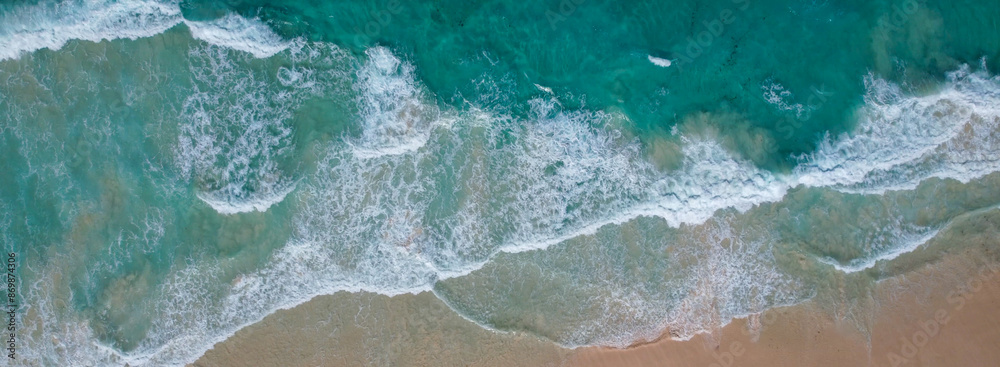 Aerial view of turquoise waves gently crashing onto a sandy beach. Aerial view of turquoise waves gently crashing onto a sandy beach.