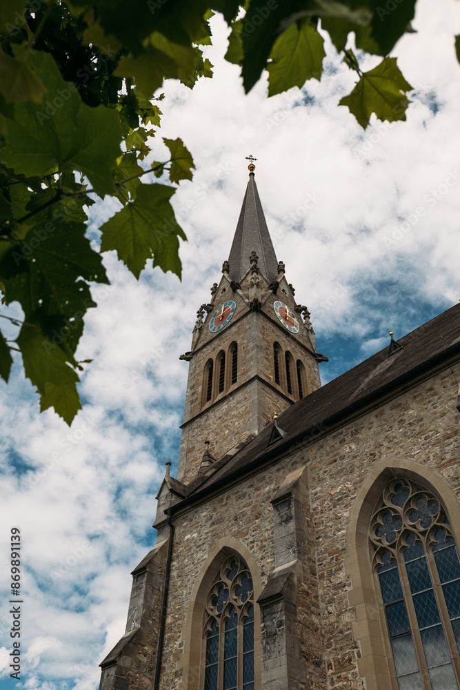 Stately Church Tower in Liechtenstein, showcasing ancient architecture and cultural heritage against Cloudy Sky Stately Church Tower in Liechtenstein, showcasing ancient architecture and cultural heritage against Cloudy Sky
