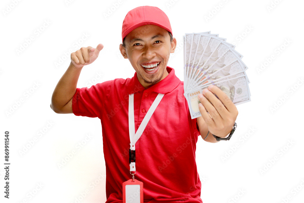 Asian delivery man or courier points towards the camera while holding money banknotes, isolated on white background. Concepts of professionalism, customer engagement, and secure monetary transactions.