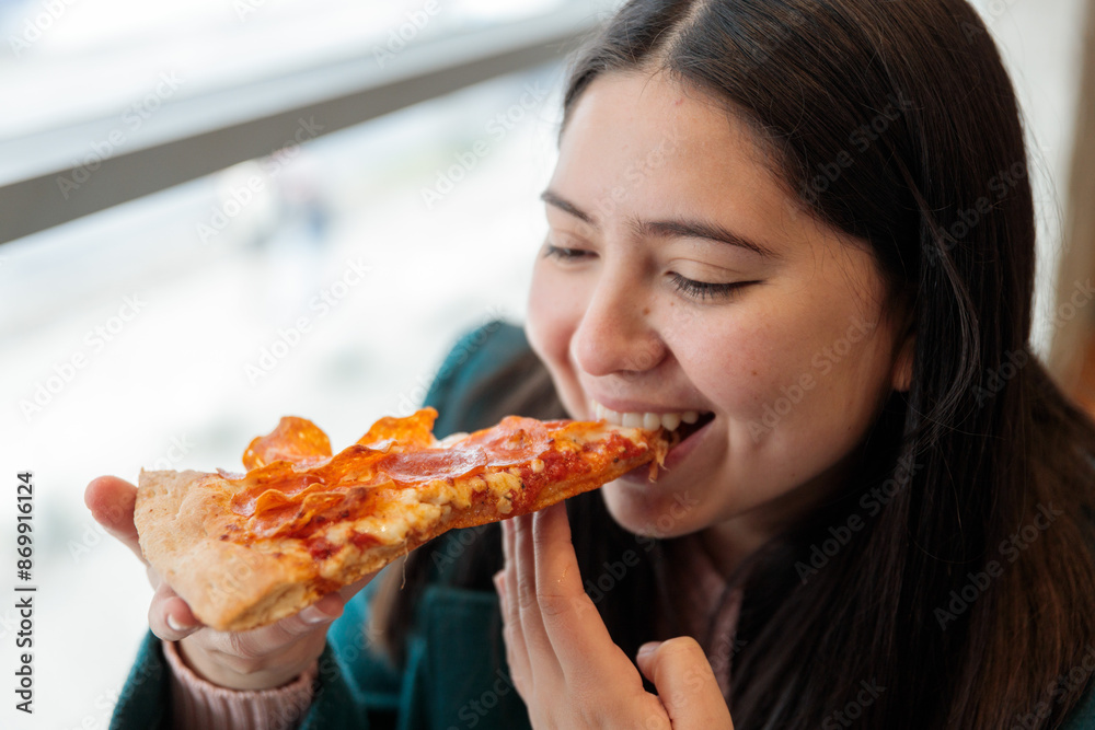Close up of smiling young latin woman eating a slice of pepperoni pizza in restaurant. Enjoying her meal with a friend Close up of smiling young latin woman eating a slice of pepperoni pizza in restaurant. Enjoying her meal with a friend