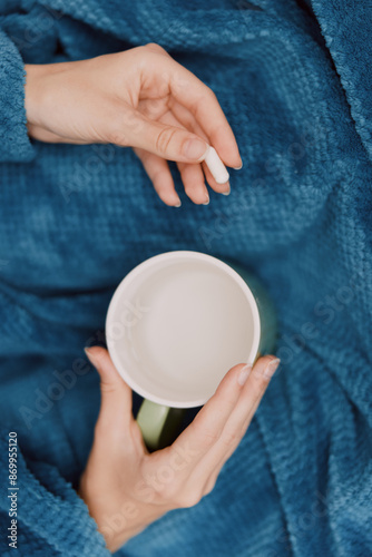 Person holding cup of coffee while sitting on blue blanket surrounded by pillows