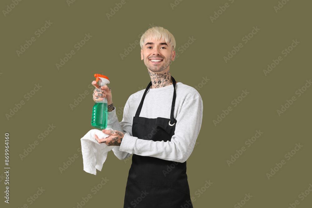 Young tattooed man with bottle of detergent and rag on green background Young tattooed man with bottle of detergent and rag on green background