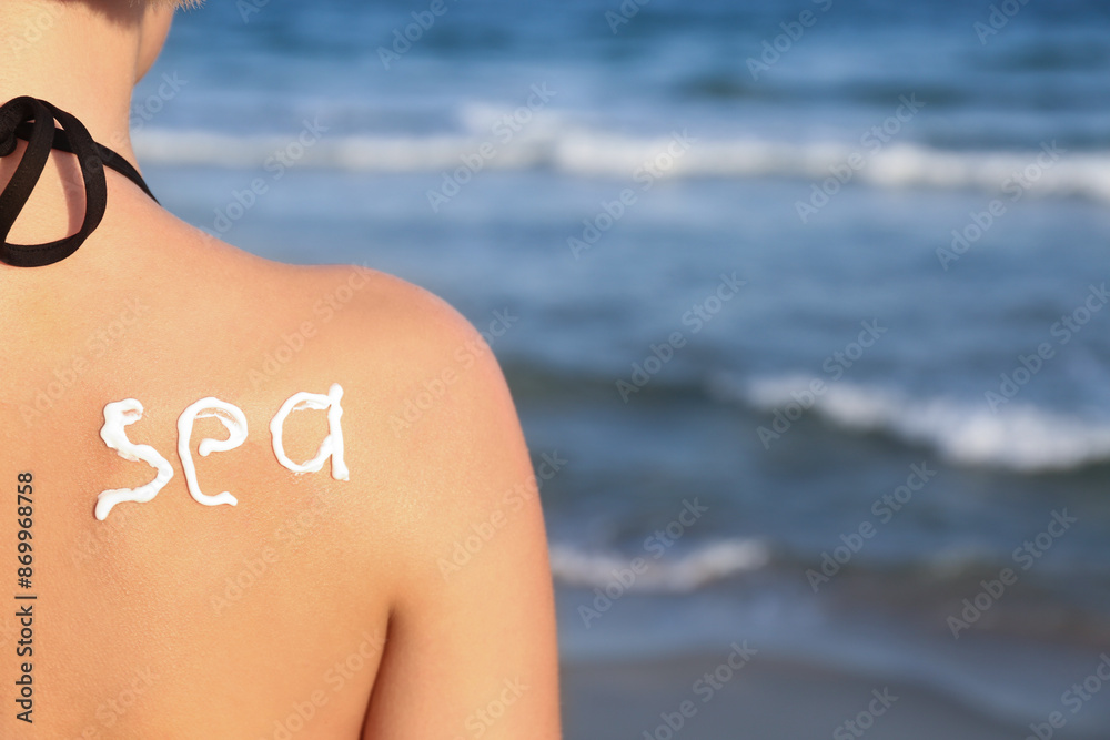 Fototapeta premium Sun protection and skincare at the beach, word sea written with sunscreen on a woman's back