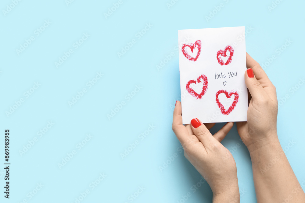 Female hands with red manicure and festive postcard on blue background. Valentine's Day celebration Female hands with red manicure and festive postcard on blue background. Valentine's Day celebration