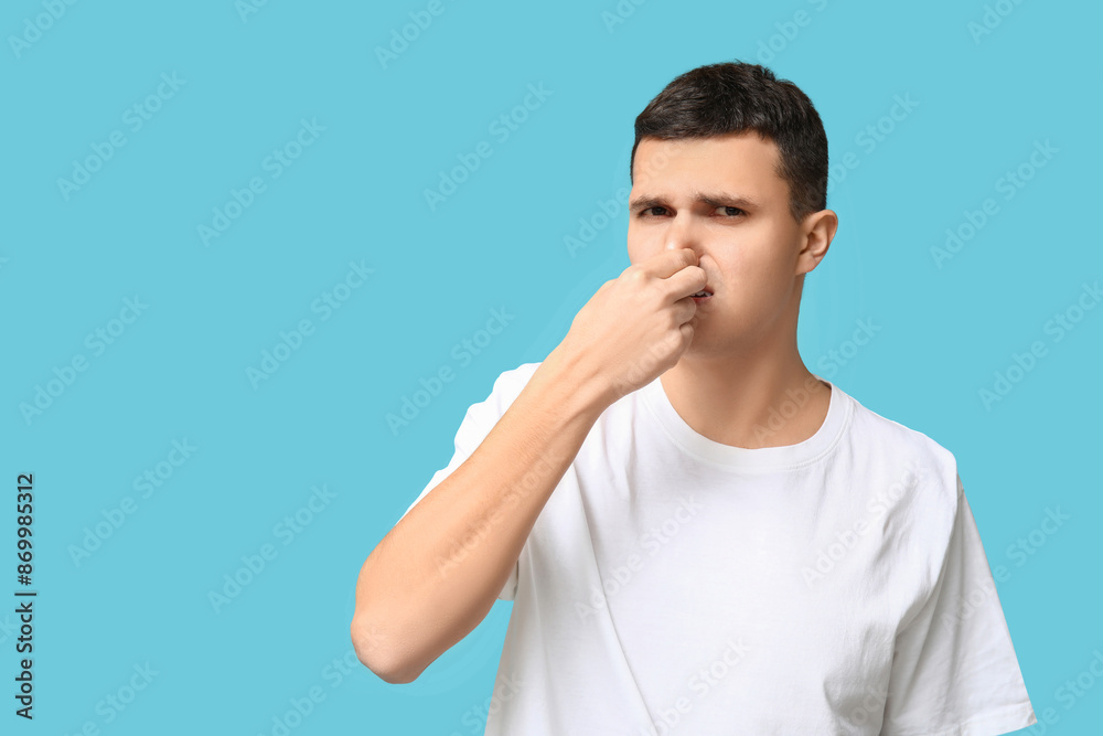 Handsome young man pinching nose because of bad smell on blue background Handsome young man pinching nose because of bad smell on blue background