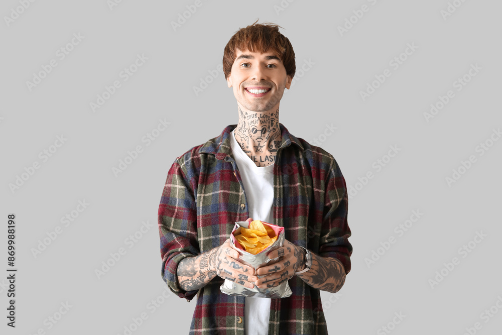 Young tattooed man with potato chips on light background