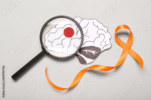 Orange ribbon, paper brain and magnifying glass on grey background. Multiple Sclerosis Awareness Month