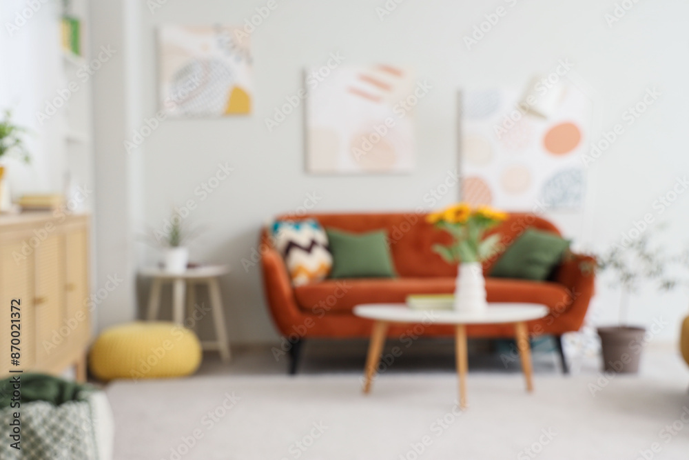 Fototapeta premium Comfortable sofa and sunflower in vase on table in living room, blurred view