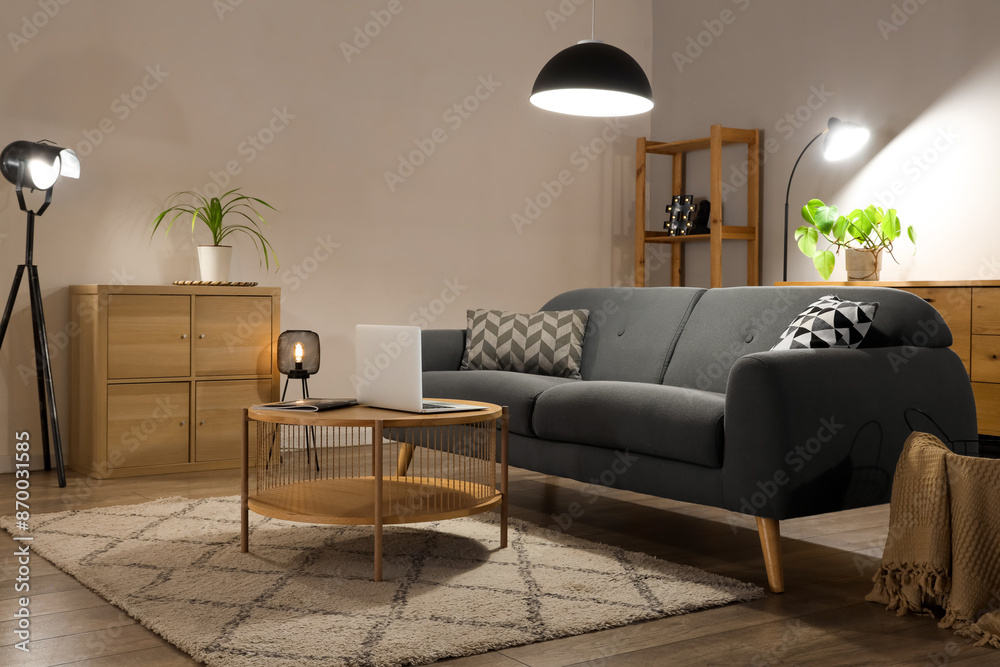 Interior of living room with comfortable sofa, table, modern laptop and glowing lamps Interior of living room with comfortable sofa, table, modern laptop and glowing lamps