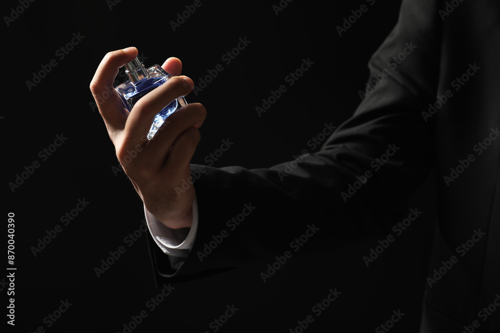 Fototapeta premium Man spraying luxury perfume on dark background, closeup
