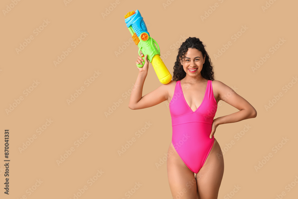 Happy African-American woman with water gun on beige background Happy African-American woman with water gun on beige background