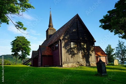 the old stave church with a steeple surrounded by greenery and blue sky at Kvernes in Averoy, Norway photo