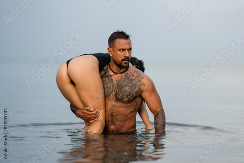 Man carrying booty woman in bikini. Sexy butt. Romantic couple kissing in the sea. Sexy couple hug on the summer beach. Love and romance couple. Muscular Hispanic man and woman in love.