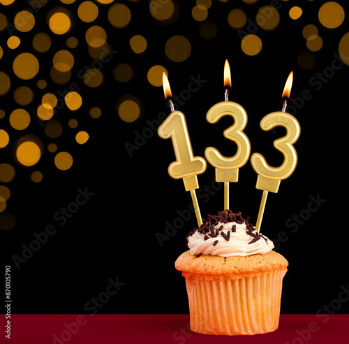 Birthday candle with cupcake - Number 133 on black background with out of focus lights photo