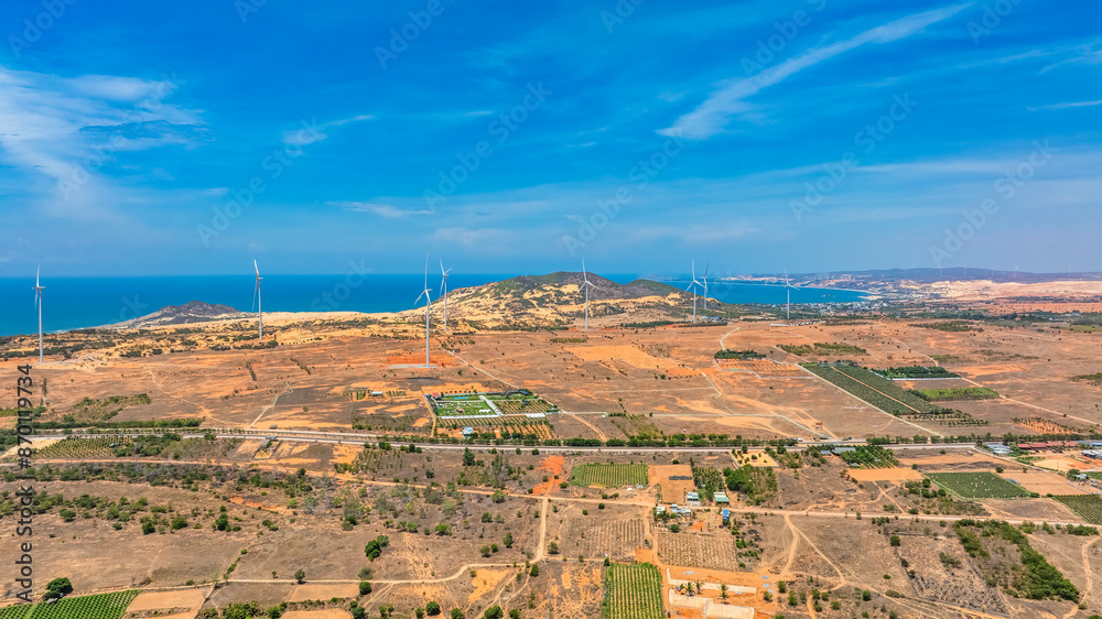 Panoramic view of wind farm or wind park, with high wind turbines for generation electricity with copy space. Green energy concept. Ocean at Bau Trang, Binh Thuan, Vietnam Panoramic view of wind farm or wind park, with high wind turbines for generation electricity with copy space. Green energy concept. Ocean at Bau Trang, Binh Thuan, Vietnam