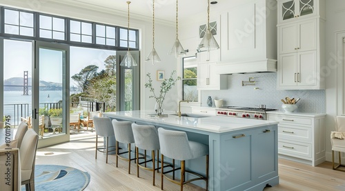 Coastal kitchen with light blue cabinets, white quartz island countertop, and barstools, featuring large windows overlooking the ocean 