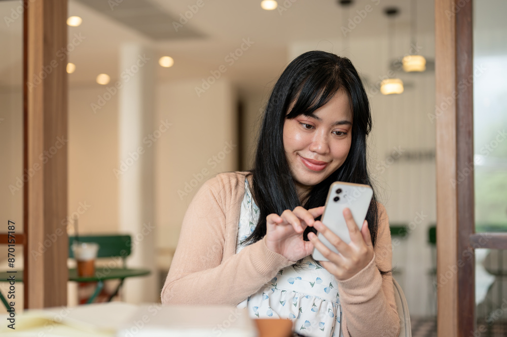 A beautiful Asian woman scrolling on her phone while relaxing in a coffee shop. A beautiful Asian woman scrolling on her phone while relaxing in a coffee shop.