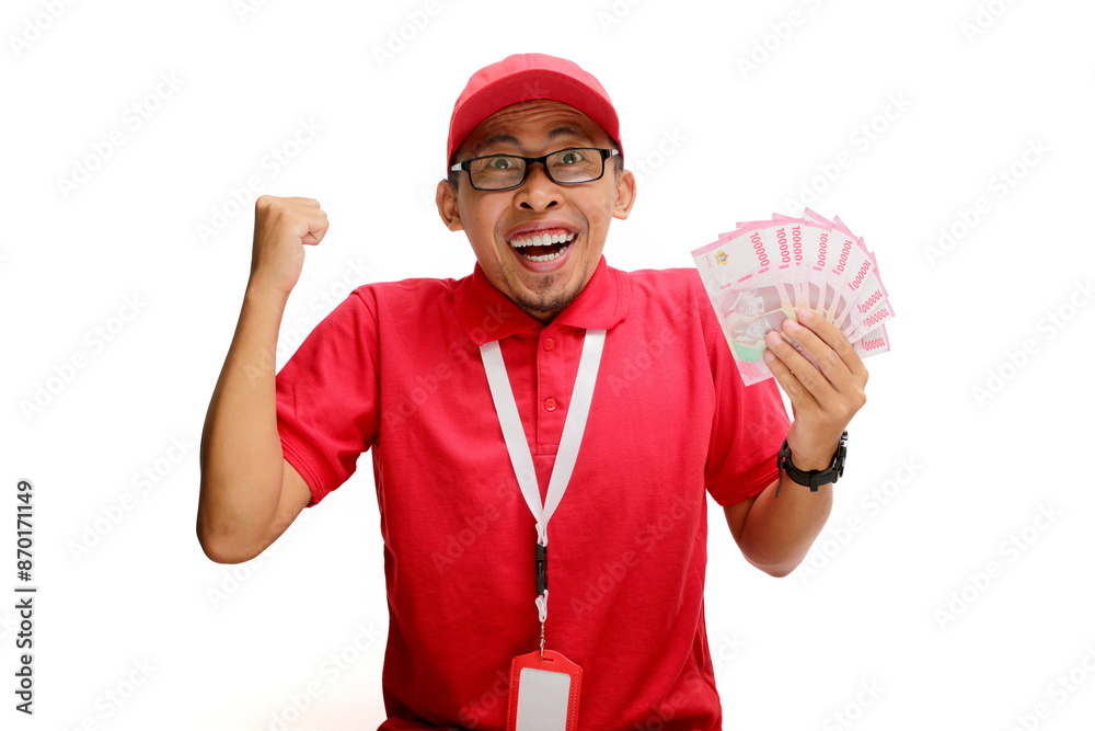Excited Asian delivery man or courier raises his fist in triumphant YES gesture while holding money banknotes in his hand, isolated on white background. Concepts of victory, financial gains, triumphs Excited Asian delivery man or courier raises his fist in triumphant YES gesture while holding money banknotes in his hand, isolated on white background. Concepts of victory, financial gains, triumphs