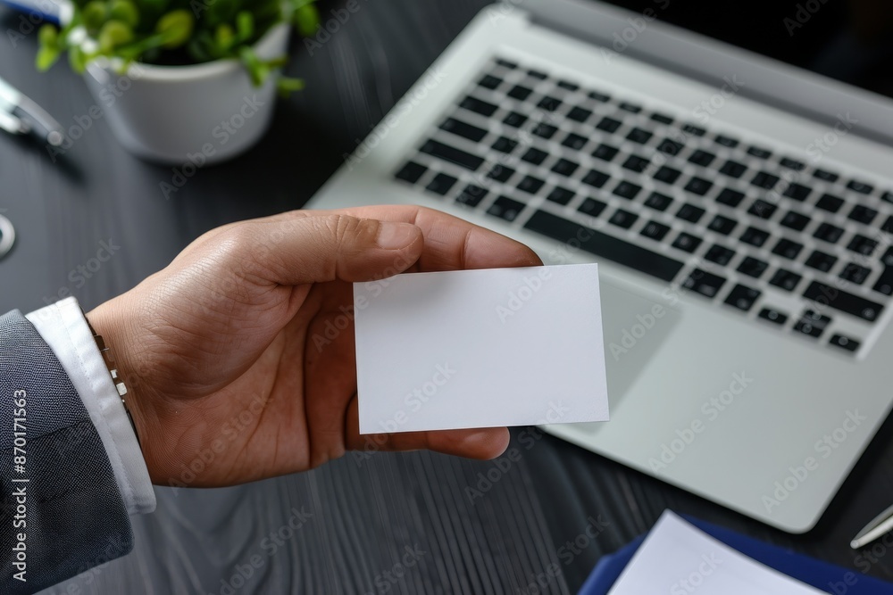 Hand Holding Blank Business Card Over Laptop Keyboard in Office for Professional Branding