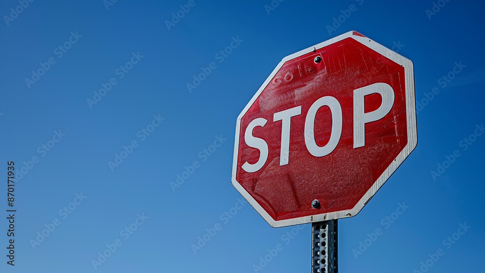 Red and white stop sign on the side of the road isolated on a blue sky background. Red and white stop sign on the side of the road isolated on a blue sky background.