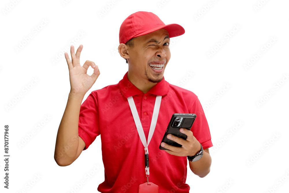 Asian delivery man or courier smiling and showing the OK gesture and winking to the camera while holding a phone. Isolated on a white background Asian delivery man or courier smiling and showing the OK gesture and winking to the camera while holding a phone. Isolated on a white background