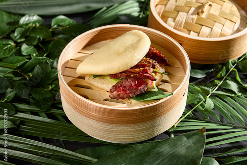 Delicious Beef Roast Bao Bun in Bamboo Steamer on Natural Leaf Background photo