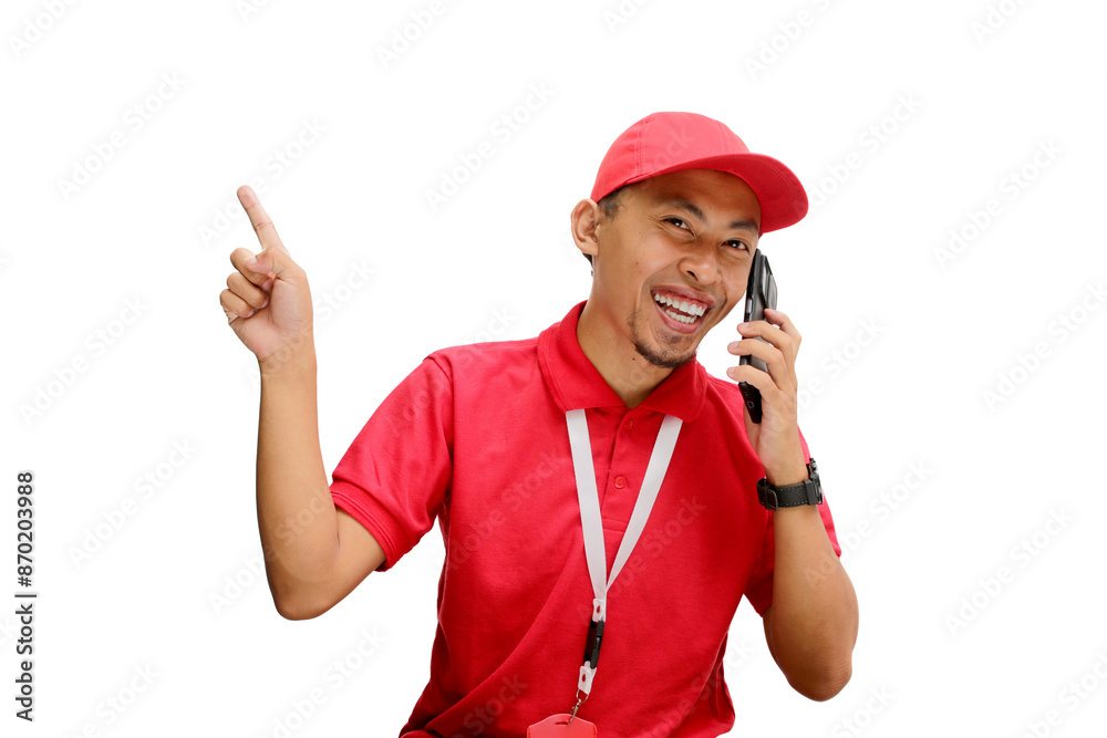 An excited Asian delivery man or courier pointing left at copy space while having an engaging phone call. Isolated on a white background An excited Asian delivery man or courier pointing left at copy space while having an engaging phone call. Isolated on a white background