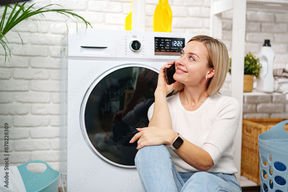 Woman Using Smartphone Near White Laundry Machine in Home Laundry Room Woman Using Smartphone Near White Laundry Machine in Home Laundry Room